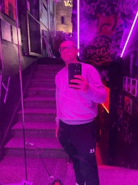 a man taking a selfie in front of a neon sign